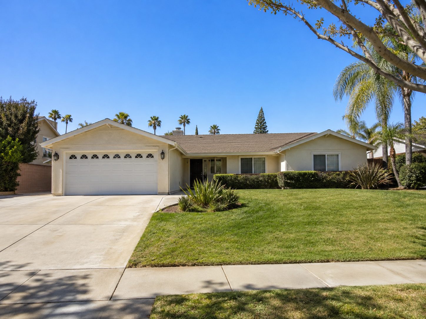 Front of a ranch house with a white two car garage door under a gable, beside a hedge and lawn