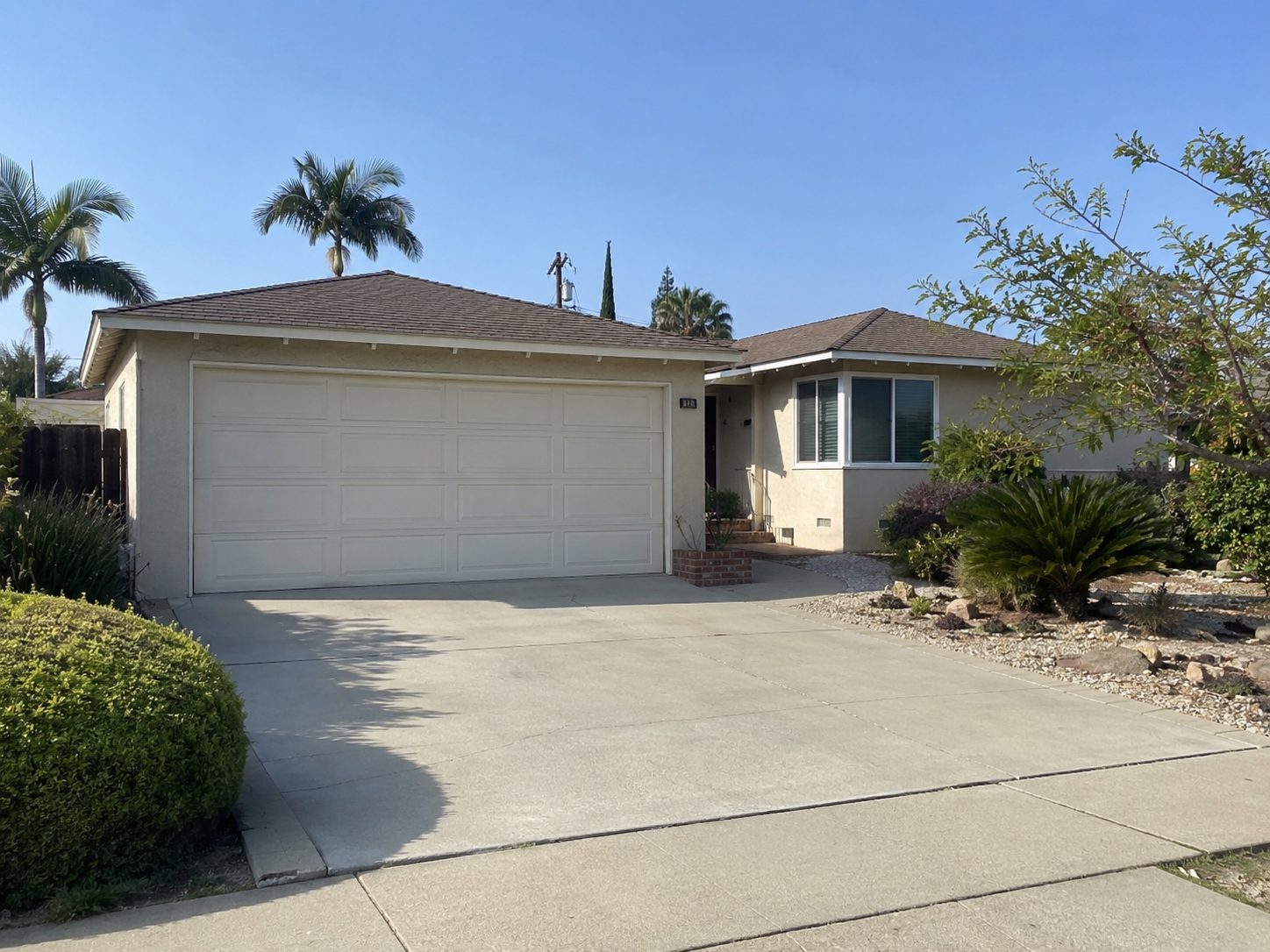 Front of a single storey house with a wide concrete driveway and a rock and gravel garden along the right side