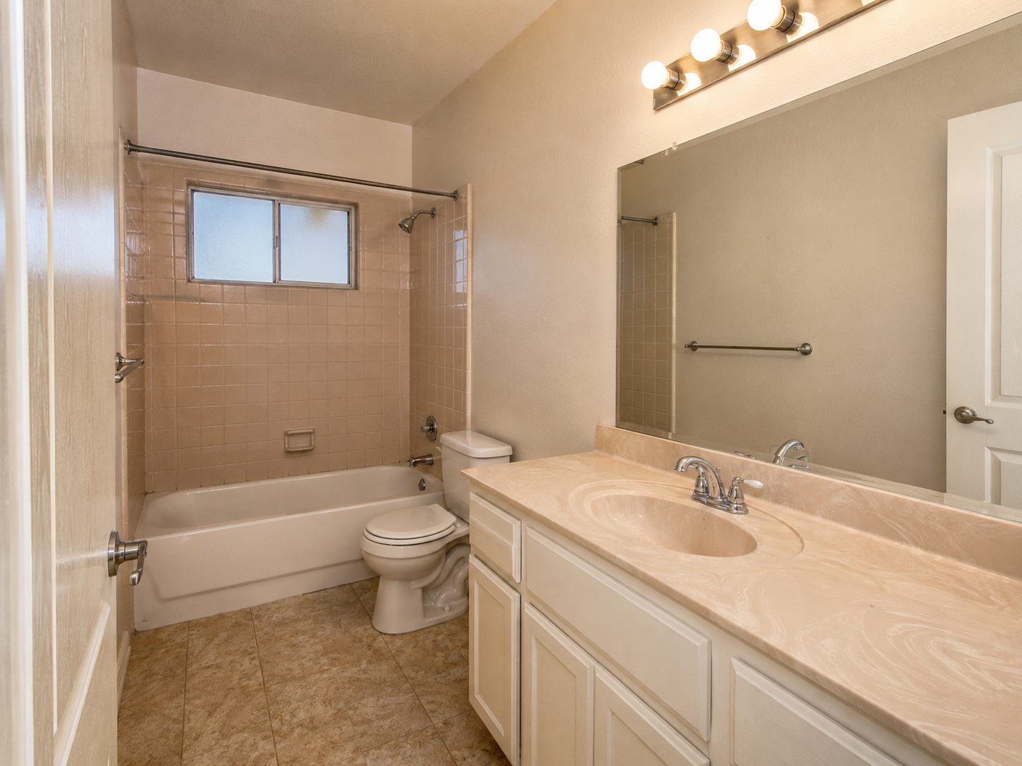 Bathroom with beige square tile, a white vanity, and a large mirror before remodeling