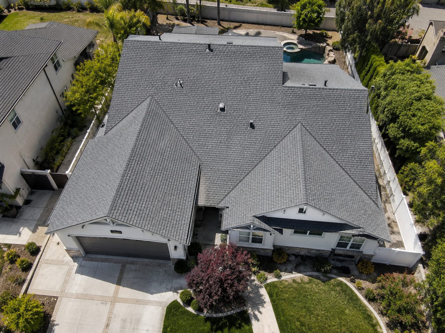 Aerial view of a single story house with a newly installed grey architectural shingle roof, ridge vents, and clean hip and valley lines