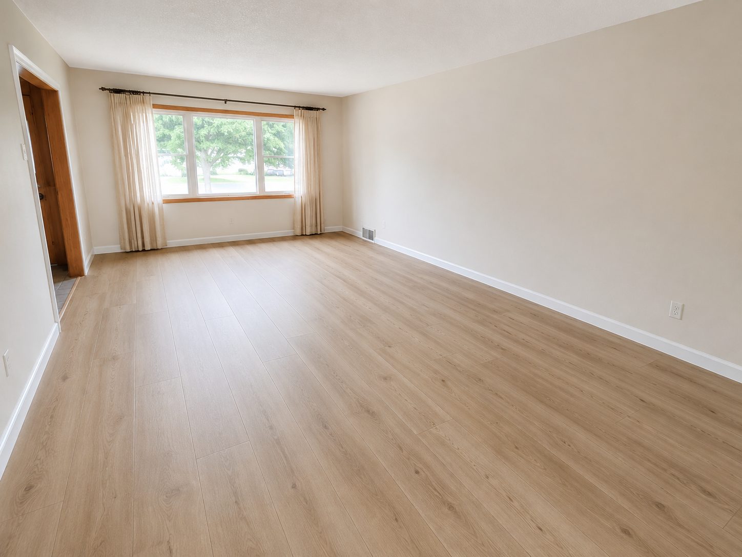 Living room with new light oak plank flooring laid wall to wall and the baseboard reset