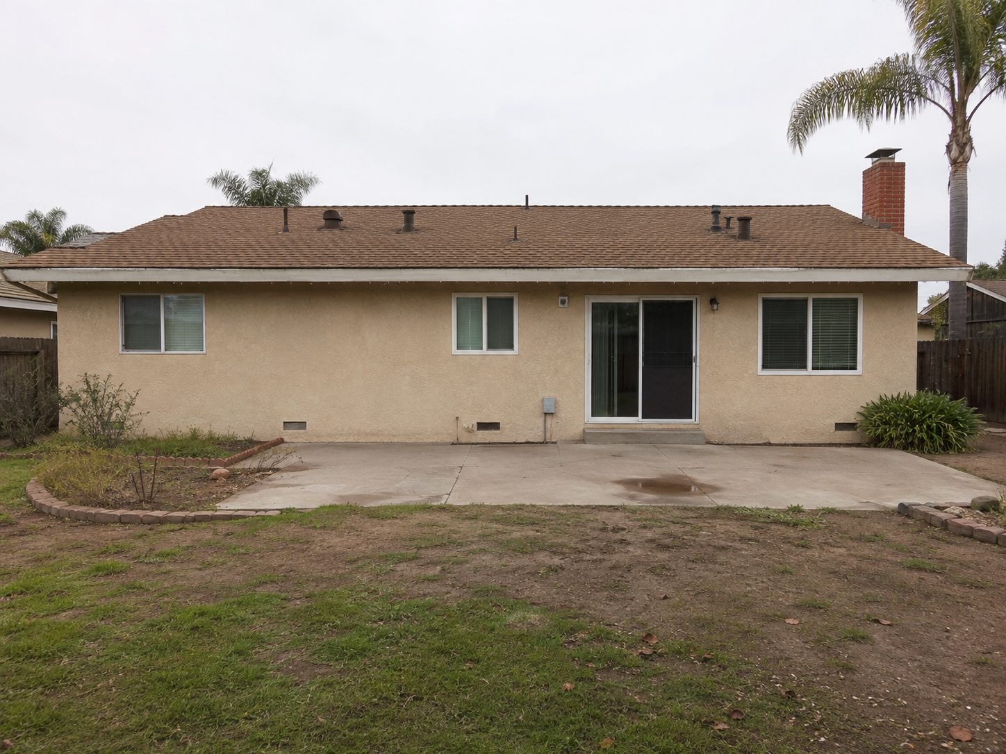 Rear elevation of a house with an empty concrete patio and thin worn grass