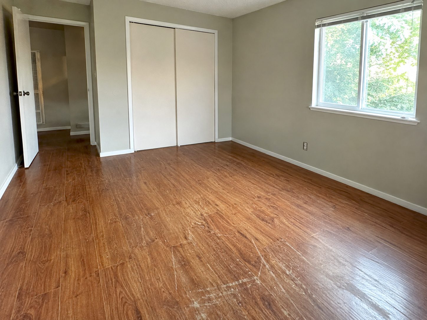 Bedroom with worn dark laminate flooring running to the baseboards