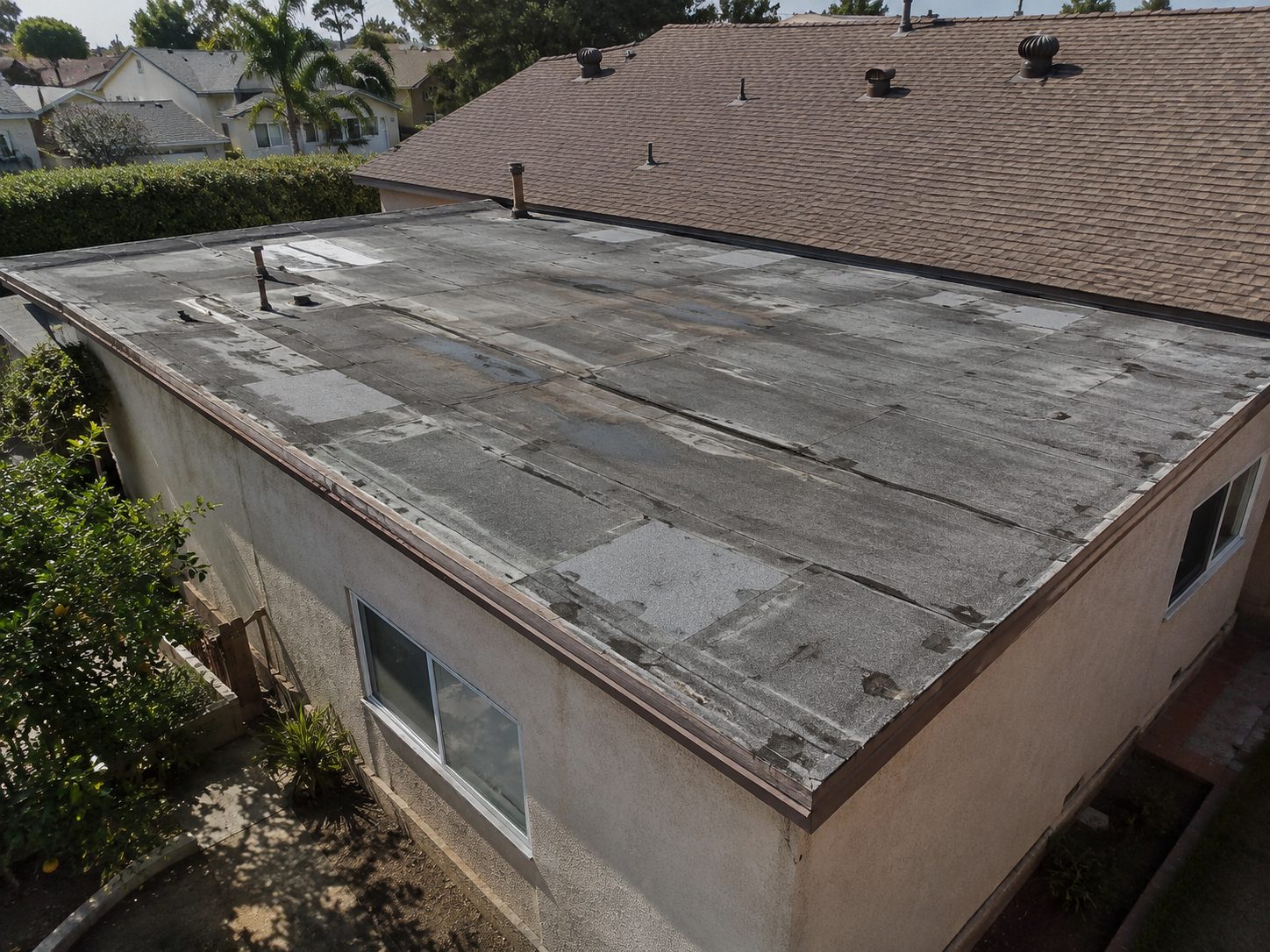 Weathered flat roof with patched seams and blistered coating across the low slope deck