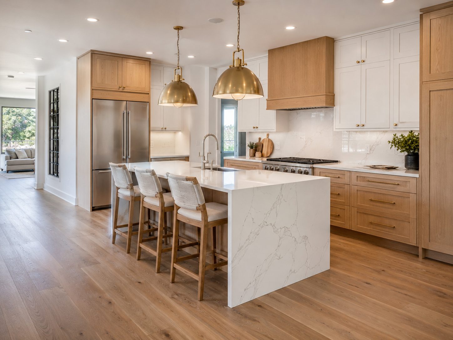 Open kitchen with white oak cabinetry, a marble waterfall island with three woven counter stools, brass dome pendants, and a wood hood over a stainless range