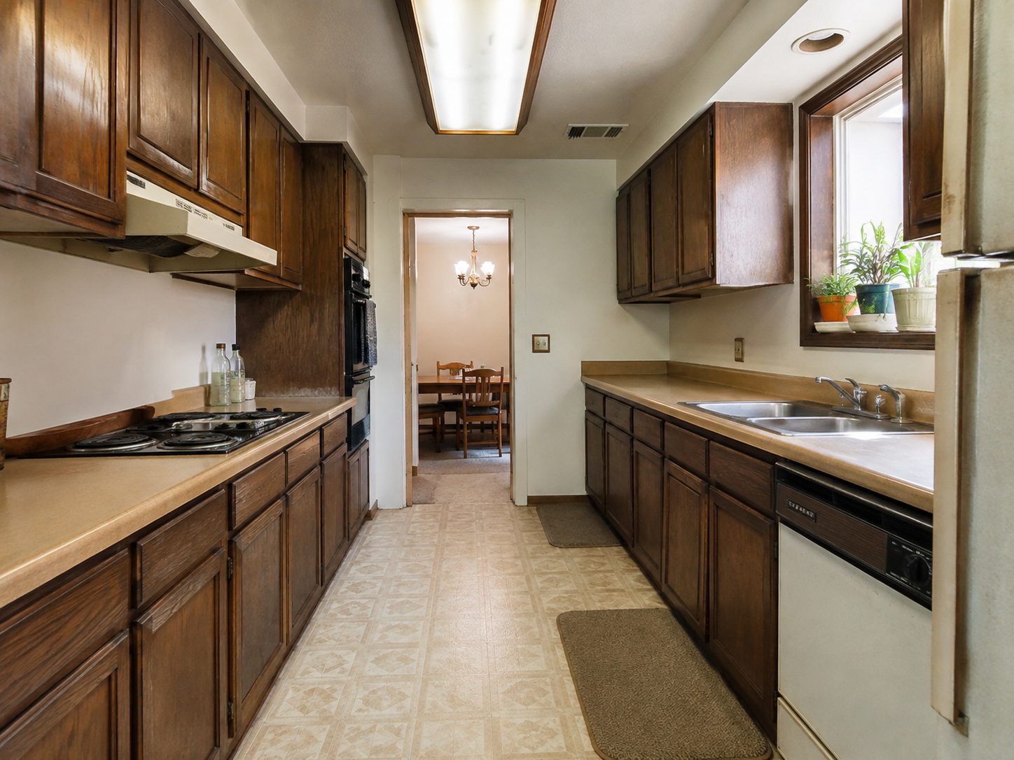 Narrow galley kitchen with dark wood cabinets and beige flooring before remodeling