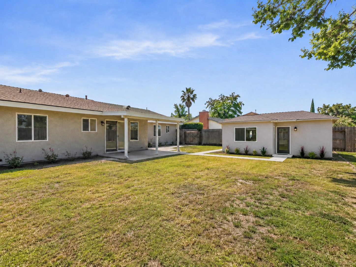 The same rear yard with a detached ADU built on the lawn, its own entry door, windows, walkway, and planting