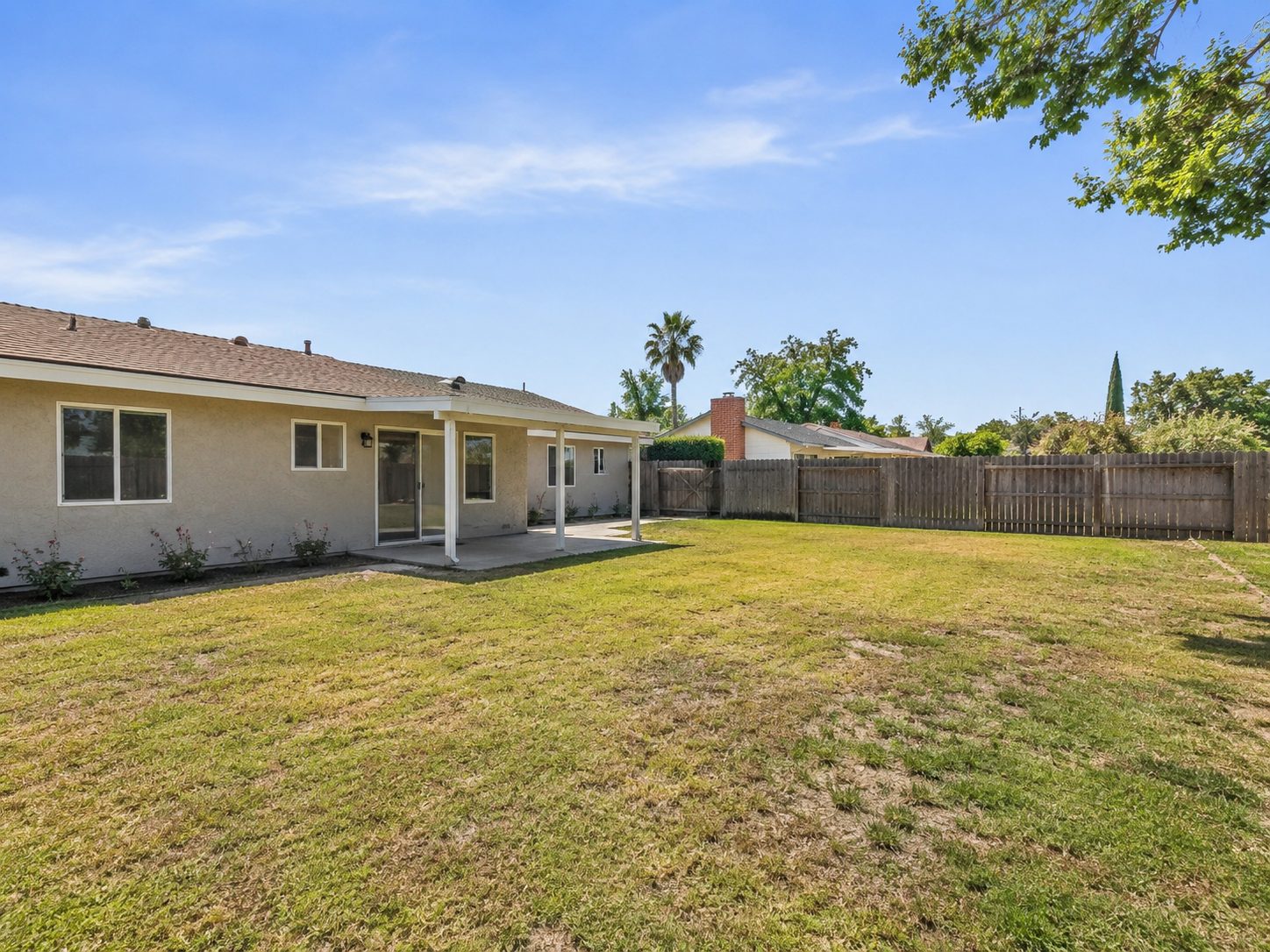Rear yard of a house with a covered patio and an empty stretch of lawn running to a wood fence